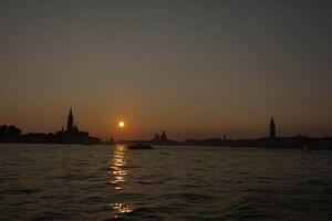 Sun setting behind venetian skyline from the water photo