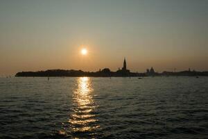 Sun setting on the horizon, creating a golden path on the sea in venice photo