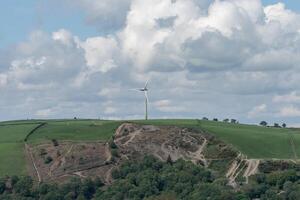 Lone wind turbine on a green hill under cloudy sky photo