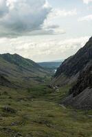 Lush green valley between steep rocky slopes under a dramatic cloudy sky photo