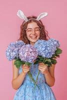 Joyful girl with bunny ears holding blue hydrangeas in front of pink backdrop photo