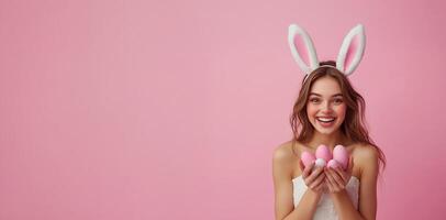 Young woman wearing bunny ears holds colorful eggs against a pink background for celebration photo