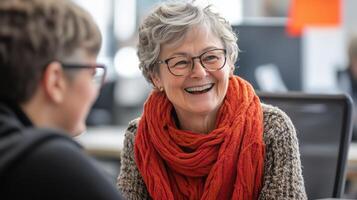 Woman with gray hair laughing while chatting with a friend in a bright office setting photo