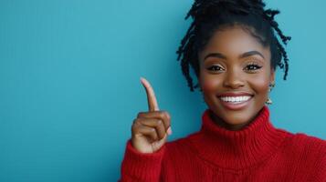 Young woman in a red sweater smiles and points upward against a blue background photo