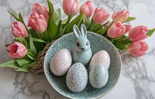 Colorful Easter eggs in a decorative bowl with a bunny figurine and fresh pink tulips photo