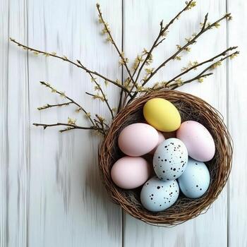Colorful eggs arranged in a decorative nest with blooming branches on a light wooden surface photo