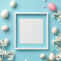Colorful eggs and spring flowers surrounding a blank frame on a blue background for seasonal display photo