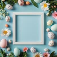 Colorful Easter eggs and flowers arranged around a blank frame on a blue background photo