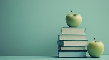 Stacked books with green apples on top against a solid background photo