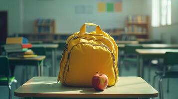 Bright yellow backpack and red apple on wooden desk in classroom during sunny school day photo