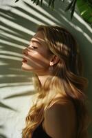 Woman with long hair illuminated by sunlight and shadow from palm leaves in a serene indoor setting photo
