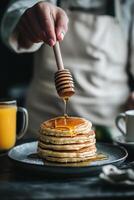 Delicious pancakes with honey drizzle served on a dark table with orange juice photo