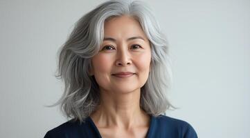 Elegant woman with silver hair smiles warmly in a modern indoor setting across a calm background photo