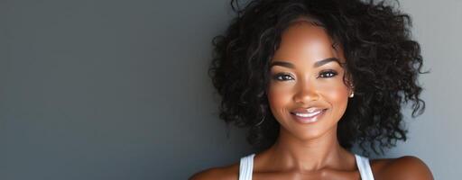 Smiling woman with curly hair posing against a gray background in natural light photo