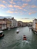 Scenic Venice Grand Canal with Boats at Sunset in Autumn. Enjoy a tranquil evening scene of a Venice canal with boats gently gliding under a colorful sunset sky, capturing the charm and romance of this iconic Italian city. photo