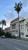 Classic European architecture in the heart of Nice, France, with palm trees lining the road. The elegant building stands under a soft evening sky, evoking a luxurious and tranquil atmosphere. Perfect for travel, lifestyle, and architecture themes. photo