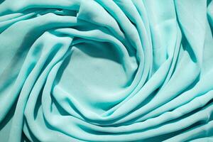Spiral Twisted Turquoise wavy crumpled fabric with little sparkling dust and copy space in center, abstract fabric background. photo
