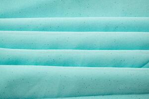 Folded Turquoise wavy crumpled fabric with little sparkling dust, texture and background. photo