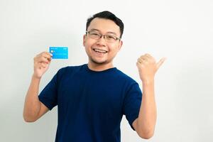 Happy asian man hold credit card with pointing pose. Banking, Financial isolated background, blue color concept. photo