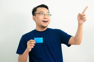 Smiling asian man hold credit card with pointing pose. Banking, Financial isolated background, blue color concept. photo
