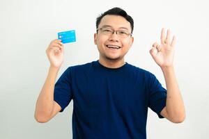 Happy asian man blue tshirt hold credit card with Ok hand sign pose. Banking, Financial isolated background, blue color concept. photo