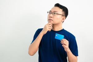 Thinking asian man hold and pointing credit card. Banking, Financial isolated background, blue color concept. photo