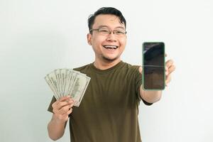 Delighted asian man hold Money and showing phone screen. Banking, Financial and technology isolated background, green color concept. photo