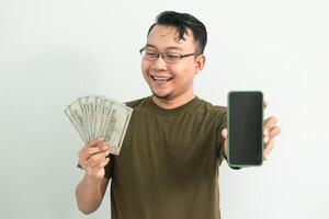 Cheerful asian man hold Money and showing phone screen. Banking, Financial and technology isolated background, green color concept. photo