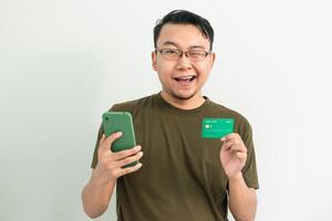Blinked asian man wear green tshirt hold credit card and phone. Banking, Financial and technology isolated white background photo