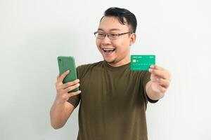Cheerful asian man wear green tshirt hold credit card and phone. Banking, Financial and technology isolated background photo
