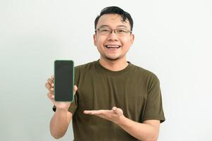 Joyful Asian man wear green tshirt pointing at phone. portrait isolated background, green color concept. photo