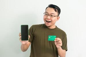 Cheerful asian man hold credit card and phone. Banking, Financial and technology isolated white background photo