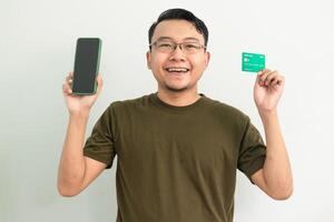 Joyful asian man wear green tshirt hold credit card and phone. Banking, Financial and technology isolated background photo