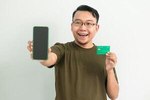Happy asian man wear green tshirt hold credit card and phone. Banking, Financial and technology isolated background photo