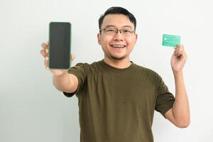 Cheerful asian man wear green tshirt hold credit card and phone. Banking, Financial and technology isolated white background photo
