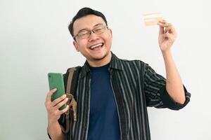 Joyful asian Student hold credit card and phone with celebrating pose. Banking, Financial and technology isolated concept. photo