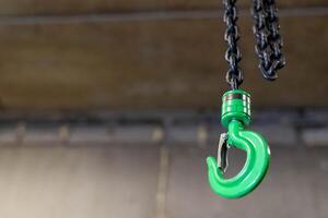 Green lifting hook hanging from chain in industrial setting photo