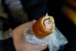 Hand holding a sausage roll wrapped in cellophane photo