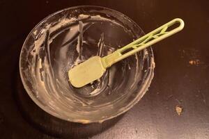 Empty mixing bowl with spatula resting on dark wooden table photo