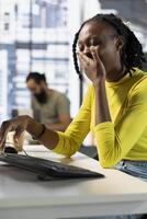 Worker in office yawning during job shift, feeling tired while looking through online business documents. Exhausted company employee being sleepy in workspace, doing tasks photo