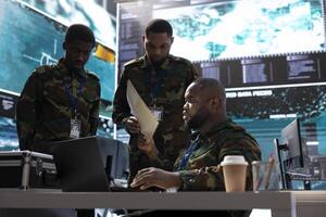 Military crew members in a control center base handle crucial information, processing live surveillance data for security protocols. Army personnel ensures reconnaissance activity vital for defense. photo