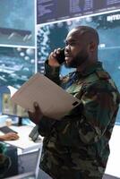 High tech military man discuss on phone call about crucial information, soldier analyzing real time data and processing intelligence. Support military missions effectively for safety. photo