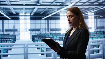 Meticulous technician doing checkup, inputting data on tablet of needed fixes in server hub housing advanced data storage infrastructure supporting critical IT workloads, camera B photo