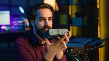 Tech content creator filming technology review of V mount battery, unpacking it and presenting specifications to audience, close up. Influencer showing charging device to subscribers, camera A photo