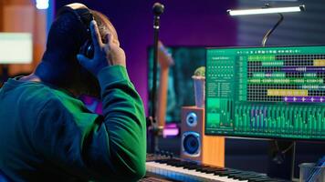 Musician playing piano keys and editing to improve sound quality of audio recordings in his home studio, putting on headset. Music producer uses midi controller to manipulate sounds. Camera A. photo