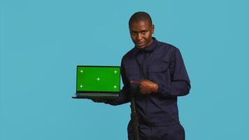 Radiant security guard working protection job presenting mockup laptop. Portrait of joyous bodyguard showcasing isolated screen notebook, isolated over studio background, camera B photo