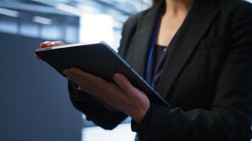 Programmer managing data center with advanced technology using digital device. Close up shot of woman walking in server room, optimizing data center tech with tablet, camera B photo