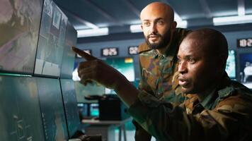 Army unit working in governmental facility next to colleague, operating surveillance monitoring tech with digital equipment. African american man doing job in base of operations, camera B photo