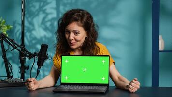 Happy content creator being sponsored by partnering brand to do green screen laptop unboxing. Upbeat technology guru does influencer marketing, doing mockup notebook product placement, camera A photo