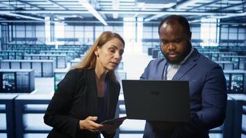 System administrators in data center overseeing server operations using notebook and tablet. Colleagues brainstorming in server hub, ensuring optimal performance and data integrity, camera B photo